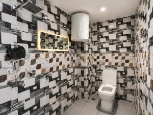 a bathroom with a toilet and a tiled wall at HOTEL SHIVAYY MAJESTIC - BHU Sundarpur Road 3km from KASHI VISHWANATH TEMPLE in Varanasi