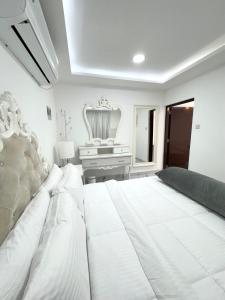 a white bedroom with a large bed and a piano at Velmora 1BR Apartment 13 in Abu Dhabi