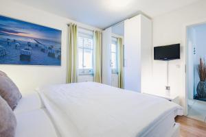 a white bedroom with a large bed and a tv at Neuland in Zingst +7 photos