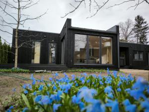 a black house with blue flowers in the foreground at Jomas & Baltic beach in Jūrmala +8 photos