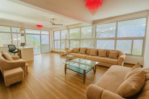 a living room with couches and a table and windows at Hotel Ambience Hill Nainital - near Bhowali in Nainital