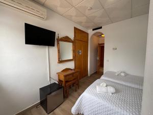 a bedroom with two beds and a television on the wall at Hostal Quinto Pino in Chipiona