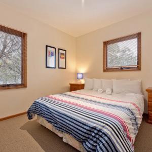 a bedroom with a bed with a striped blanket and two windows at Square Bear in Dinner Plain +2 photos