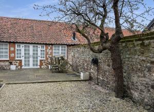 a house with a stone wall and a tree at Vine Cottage in Thornham