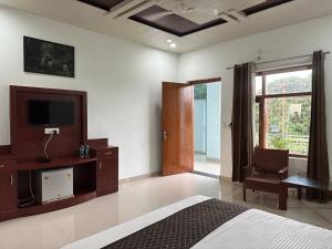 a bedroom with a bed and a tv and a chair at Kuyal Corbett Resort in Rāmnagar