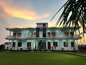 a large white house with a sunset in the background at Kuyal Corbett Resort in Rāmnagar