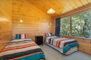 two beds in a log cabin with a window at Sea Breezes in Matarangi