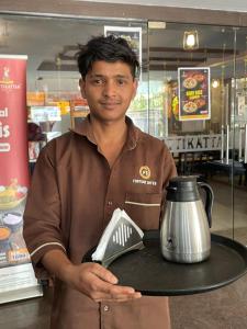 a man holding a tray with a tea kettle on it at hotel fortune city in Bangalore