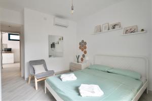 a white bedroom with a bed and a chair at Appartamentino in Bari Sardo