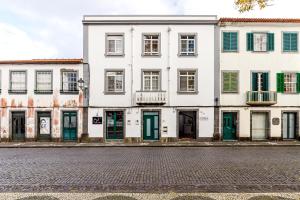 a white building with green doors on a street at Garden View Apartment in Horta