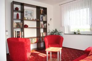 a living room with two red chairs and a book shelf at Apartment für 2, nicht für Monteure in Niederau