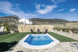 a swimming pool on a lawn with two chairs at Casa Pilar in Ronda