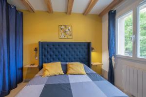 a bedroom with a blue bed with yellow walls and windows at Villa La Fenière in Payzac