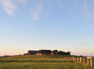 a farm in the middle of a field with a fence at Fewo Nordseeblick in Langeneß