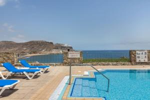 a swimming pool with blue chairs and the ocean at Su Eminencia in Mogán