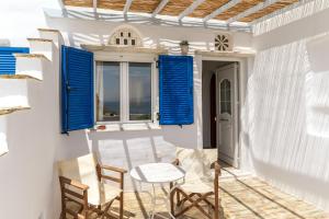 a porch with blue shutters and a table and chairs at Anemologio 304 Tinos in Agios Ioannis