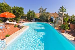 a large swimming pool with an orange umbrella and a blue pool at Casa Ginepro in Quartu SantʼElena
