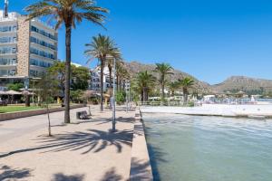 a street with palm trees next to a body of water at Taiko in Port de Pollensa