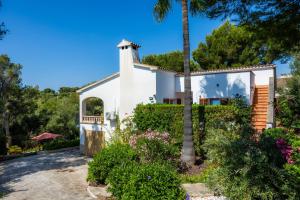 a white house with a palm tree and flowers at Casa Inés in Cala Murada
