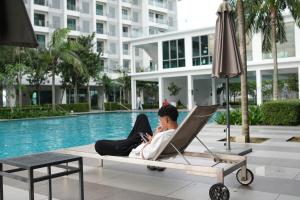 a man sitting in a chair by a pool using a cell phone at Cozy Studio Netflix Parking Self Checkin Wifi free wifi 138 in Cyberjaya