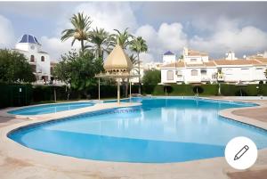 a swimming pool in a resort with palm trees and buildings at Bonito bungalow en la playa in Gran Alacant