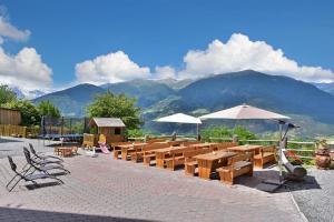 a row of wooden tables and umbrellas with mountains in the background at Birkenhof - Wohnung Ortler in Sluderno