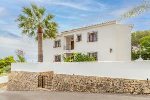 a white house with a stone wall and a palm tree at La Boniquesa in Benissa