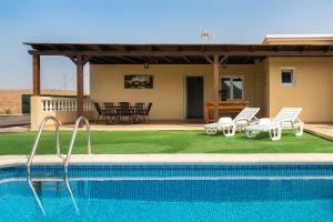 a house with a swimming pool with chairs and a patio at Villa Ralue in Tuineje