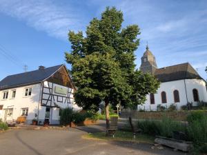 a white building with a tree and a church at Waldmomente in Schauren