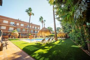 a resort yard with chairs and a pool and palm trees at Apartamentos Velor in Castelldefels