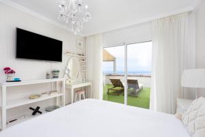 a white bedroom with a bed and a tv and a window at Sunset Costa Adeje Oceanview in Adeje