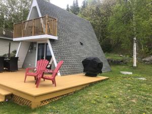 a deck with two red chairs and a balcony at Chalet Le Pointu - St-Lawrence River View in Rivière-du-Loup