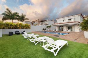 a group of white chairs sitting on a lawn in front of a house at Villa Aurora Playa La Arena in Puerto de Santiago