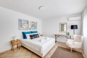 a white bedroom with a bed and a chair at VICE by Apiro Syros in Ermoupoli