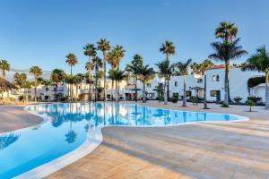 a swimming pool at a resort with palm trees and houses at Oasis Duna_Sun Fun Pool in Corralejo