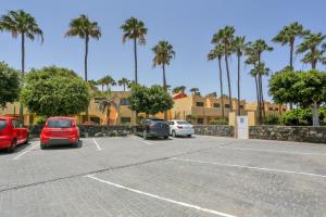 a parking lot with parked cars and palm trees at Oasis Royal F306 in Corralejo