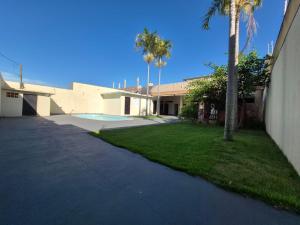 a house with a yard with palm trees and a driveway at Casa com piscina em Maringá in Maringá
