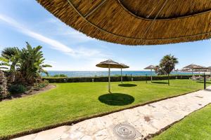 a lawn with umbrellas and the ocean in the background at Seafront Beach house Rocas del Mar in Mijas