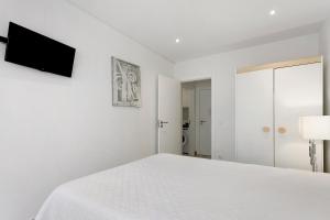 a white bedroom with a bed and a flat screen tv at Natalina T2 in Nazaré
