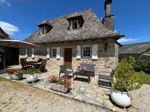 a stone house with a patio with chairs and flowers at Gite rural La Madeleine in Saint-Mathurin-Léobazel