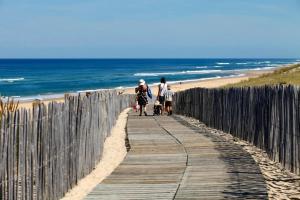 two people walking down a wooden walkway to the beach at T2 Mimizan Plage in Mimizan-Plage