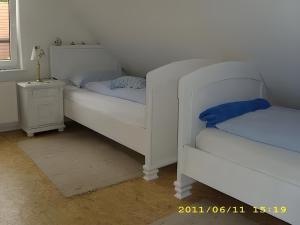 two white beds in a room with a night stand at Fennas Ferienwohnungen - Hanne in Dornumersiel +2 photos