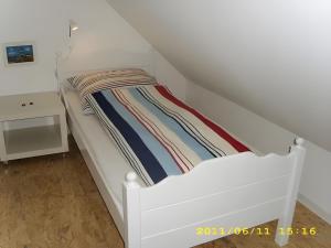 a small white bed with a striped blanket on it at Fennas Ferienwohnungen - Hanne in Dornumersiel