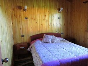 Cabañas Entremontañas Coñaripe في كونياريبي: غرفة نوم بسرير وجدران خشبية