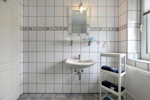 a white tiled bathroom with a sink and a mirror at Ferienwohnung Postel in Meldorf