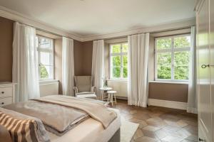 a bedroom with a bed and two windows and a chair at Schloss Kirchberg - Rose in Immenstaad am Bodensee