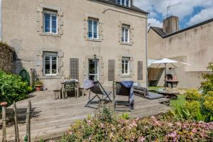 a wooden deck in front of a building with chairs and an umbrella at Maison 8 pers plein centre ville in Lesneven