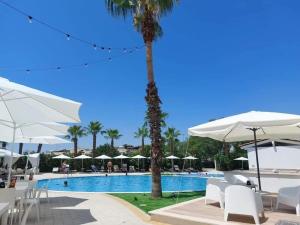 a swimming pool with white chairs and umbrellas at Pitagora Residence in Metaponto