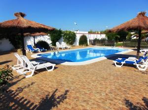 a swimming pool with white chairs and umbrellas at Cartuja Rural in Barbate