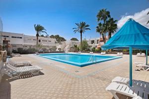 a swimming pool with chairs and a blue umbrella at Apartamento Mertxe in Arona